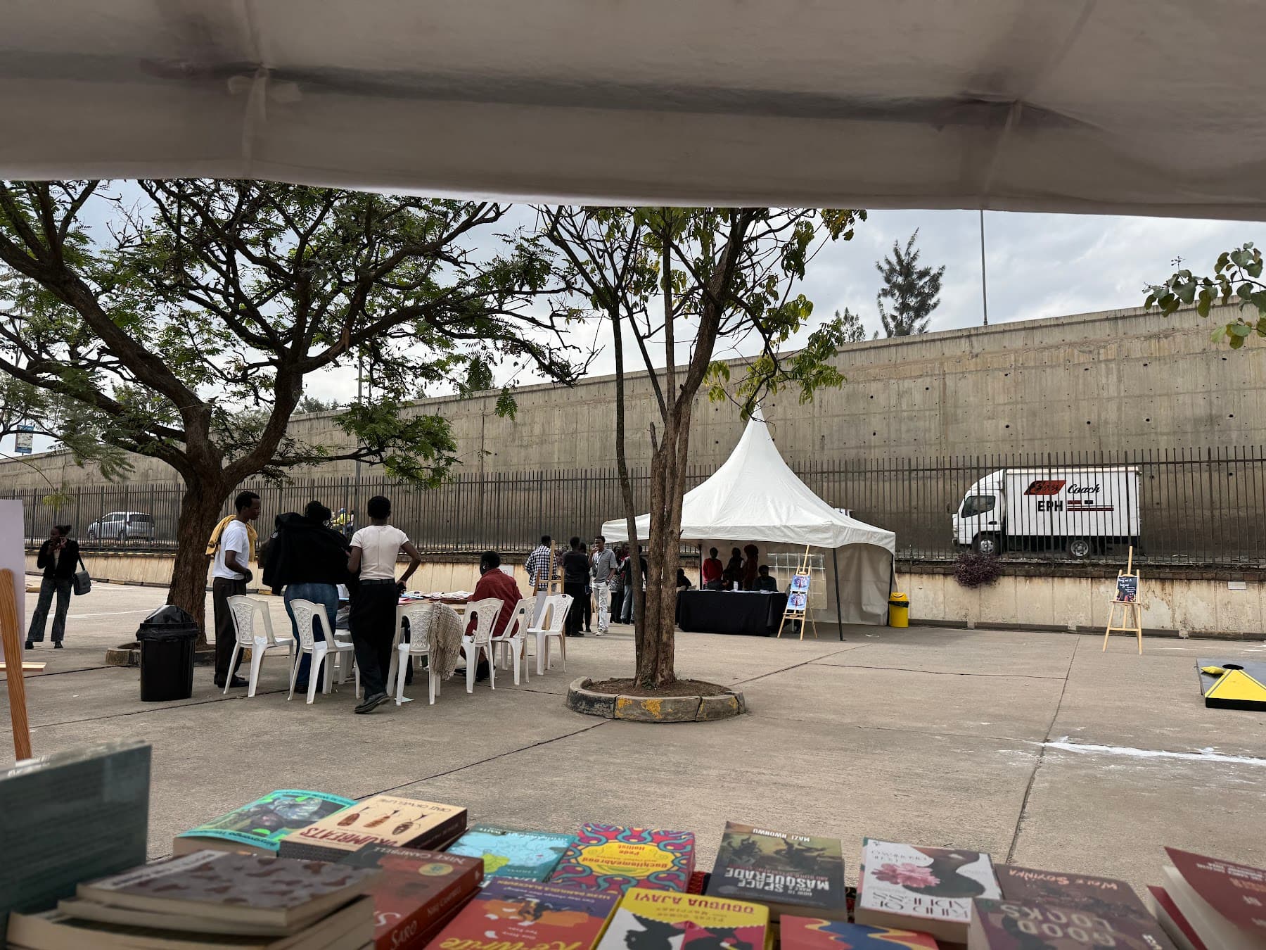 Books laid out on a table under a canopy, with the courtyard and a white tent beyond