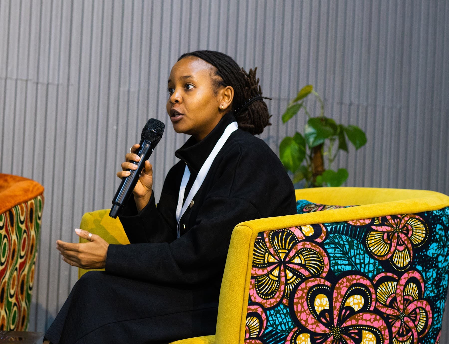A panellist speaking into a microphone from a yellow African-print armchair