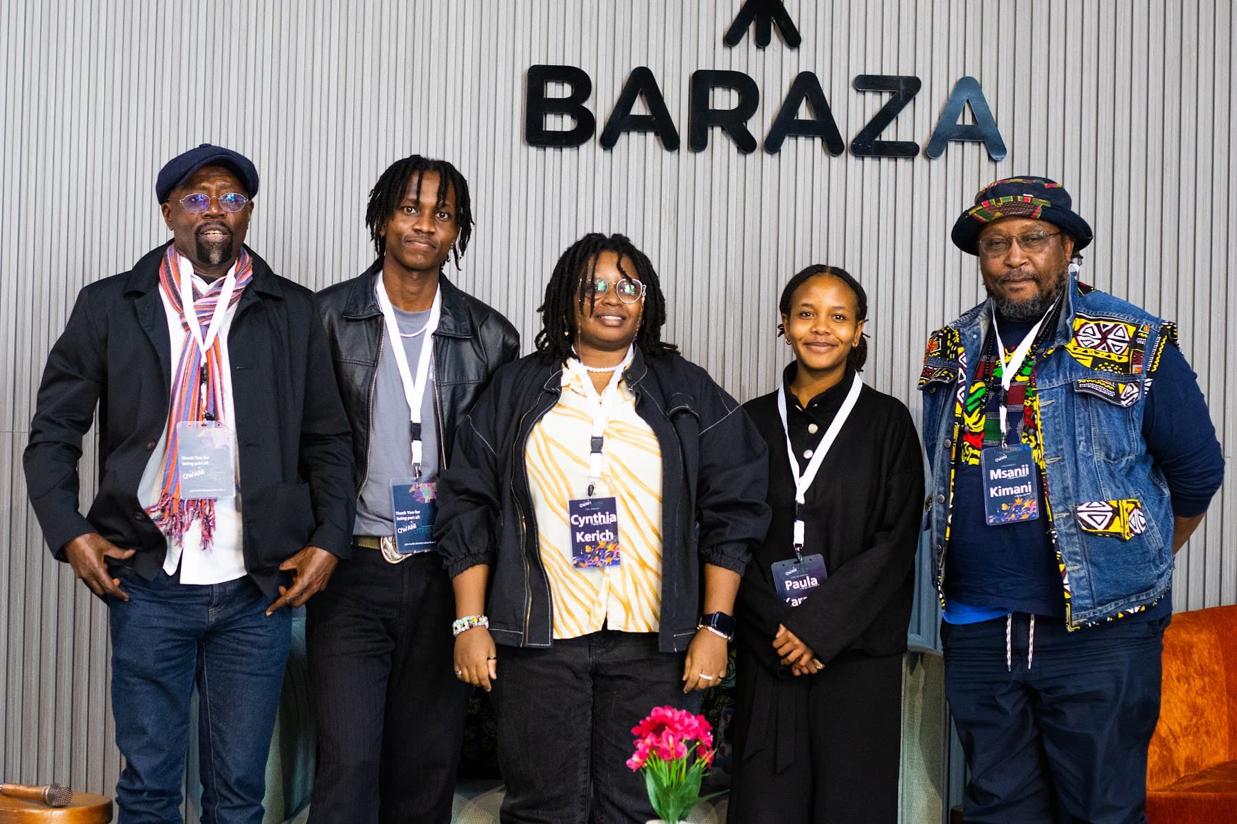 Festival participants with lanyards posing together on stage in front of the Baraza sign